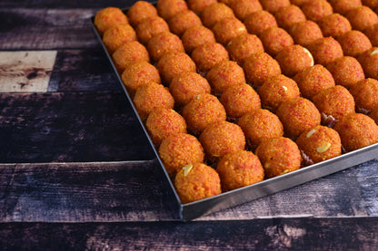 Close-up image of golden Motichoor Laddu, a traditional Indian sweet made from finely fried gram flour pearls, mixed with ghee and sugar, garnished with nuts, and shaped into round, delicious balls. Perfect for festive celebrations and special occasions.